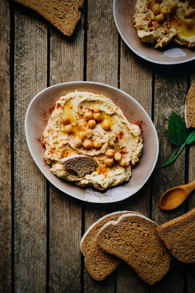 Un bol de houmous garni de pois chiches, du pain grillé à côté